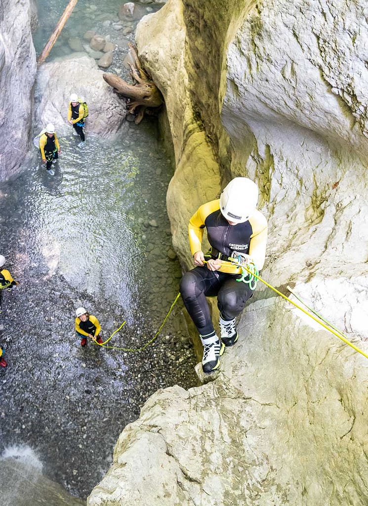 Eine Person springt in einen Canyon über Wasser, umgeben von hohen Felswänden und Bäumen.